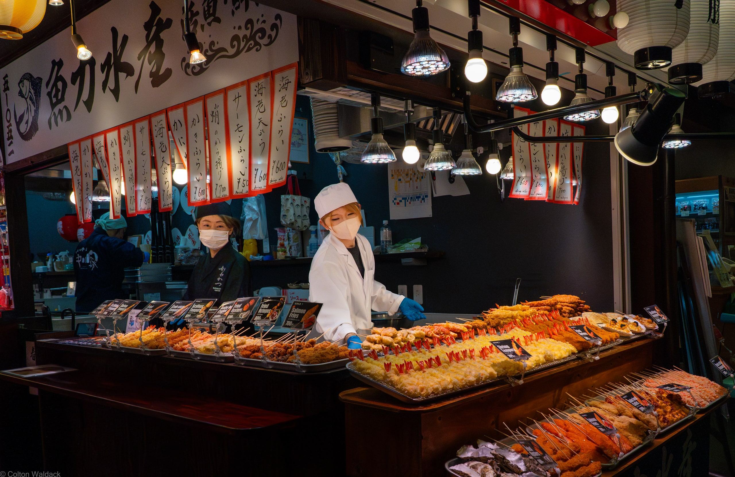 Vendors working a seafood stall under warm lights at Nishiki Market